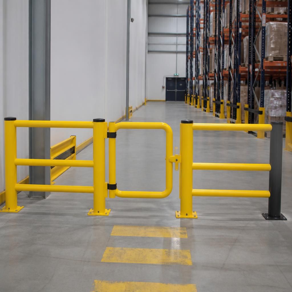 Pedestrian gate set within a fixed safety barrier beside a warehouse aisle